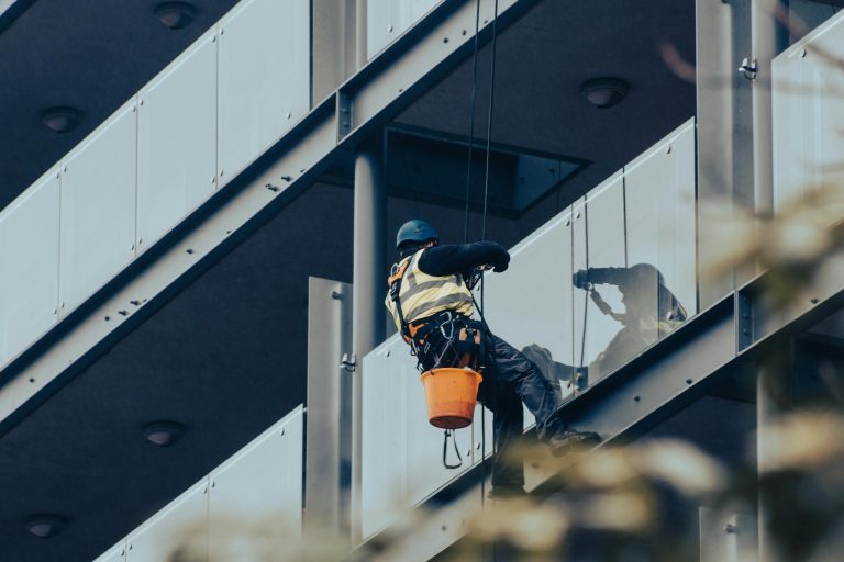 High-rise window cleaner using safety equipment on a modern building facade.