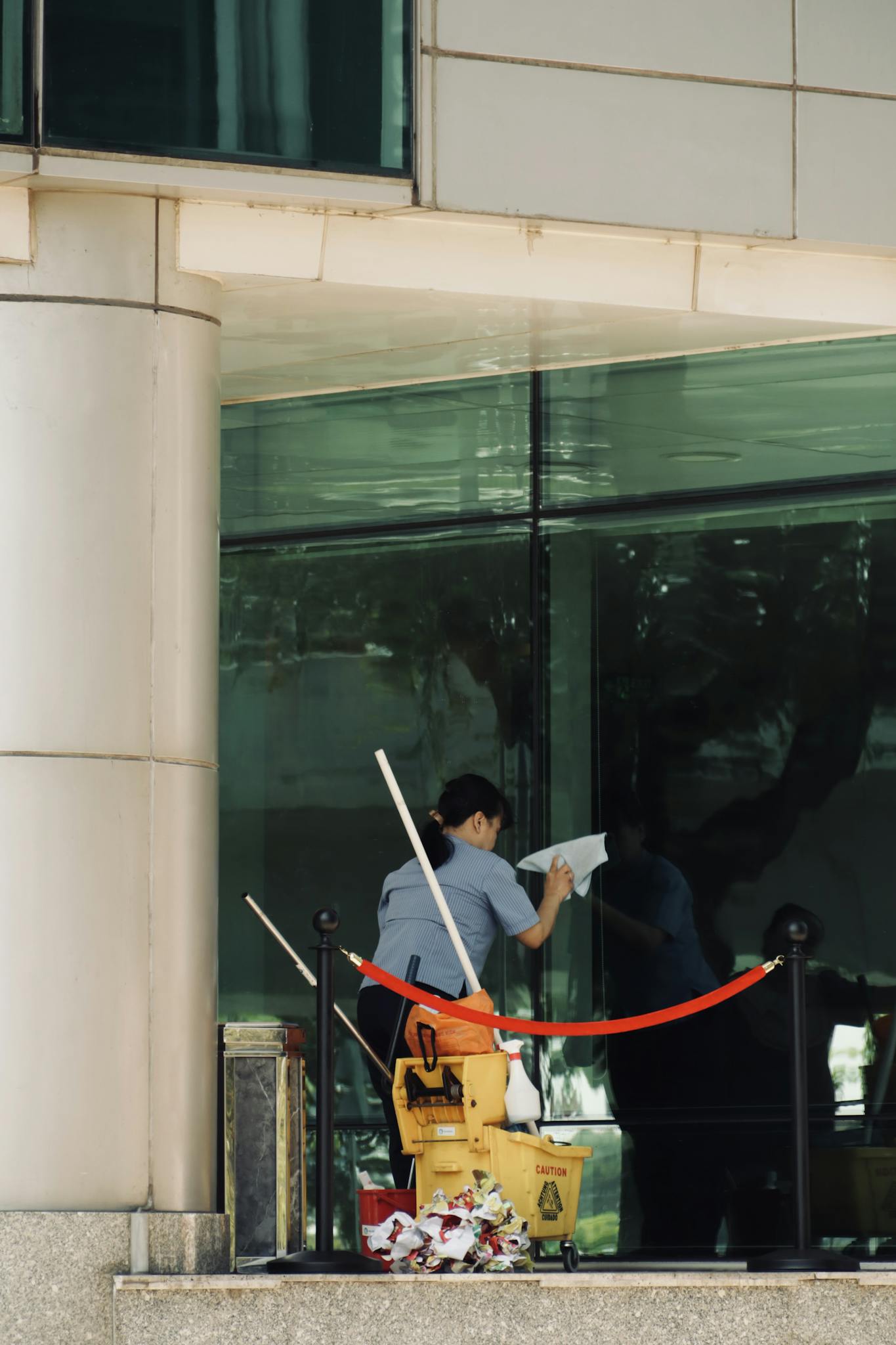 Person cleaning a glass window of a tall building with cleaning equipment visible.