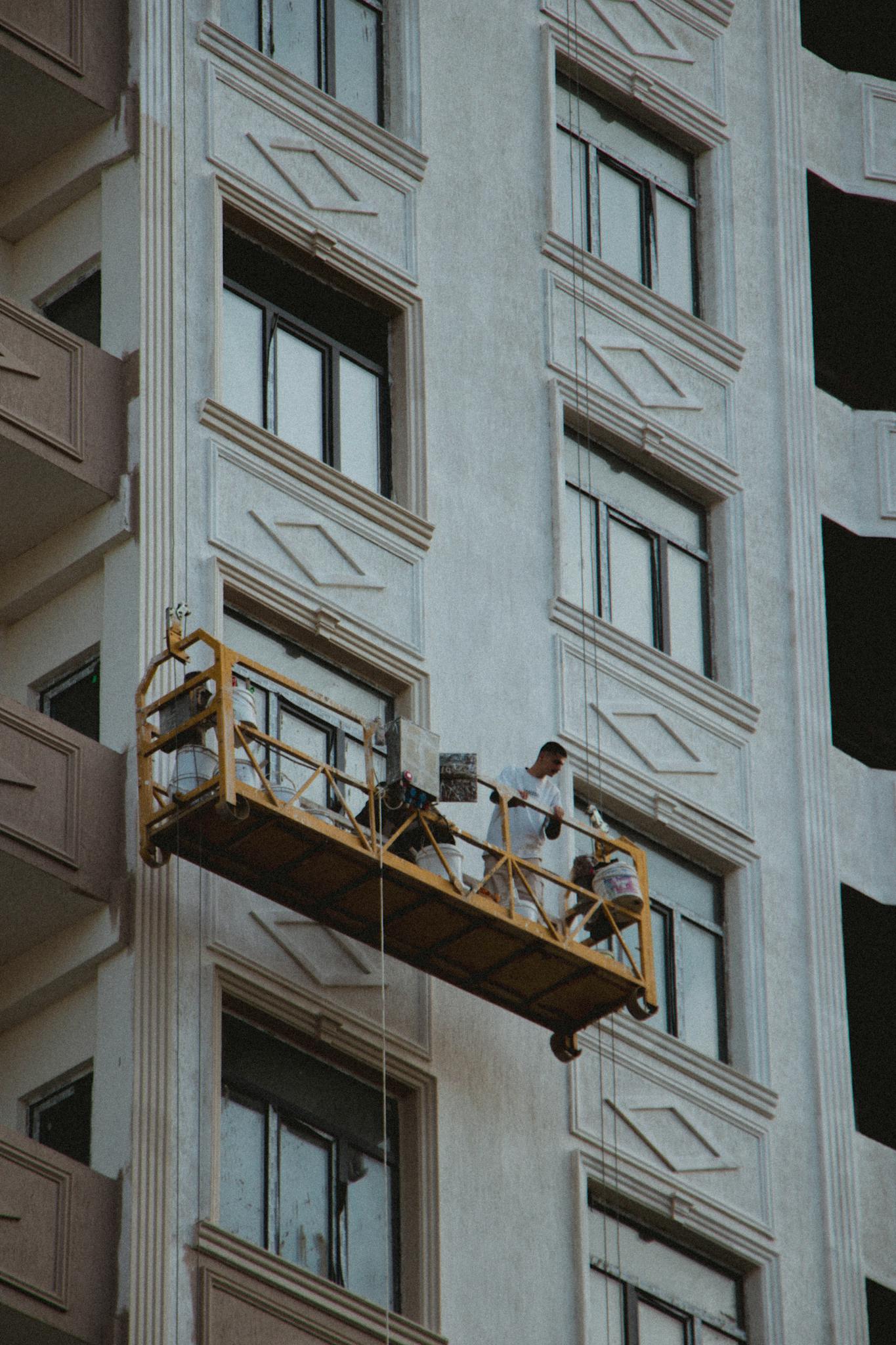 Two men are working on a building facade from a suspended scaffold, cleaning windows.