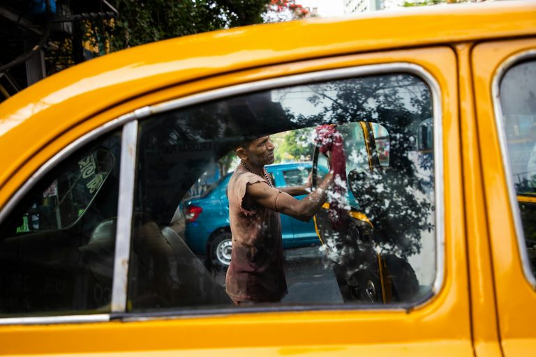 Worker cleaning yellow taxi window reflection in urban street.